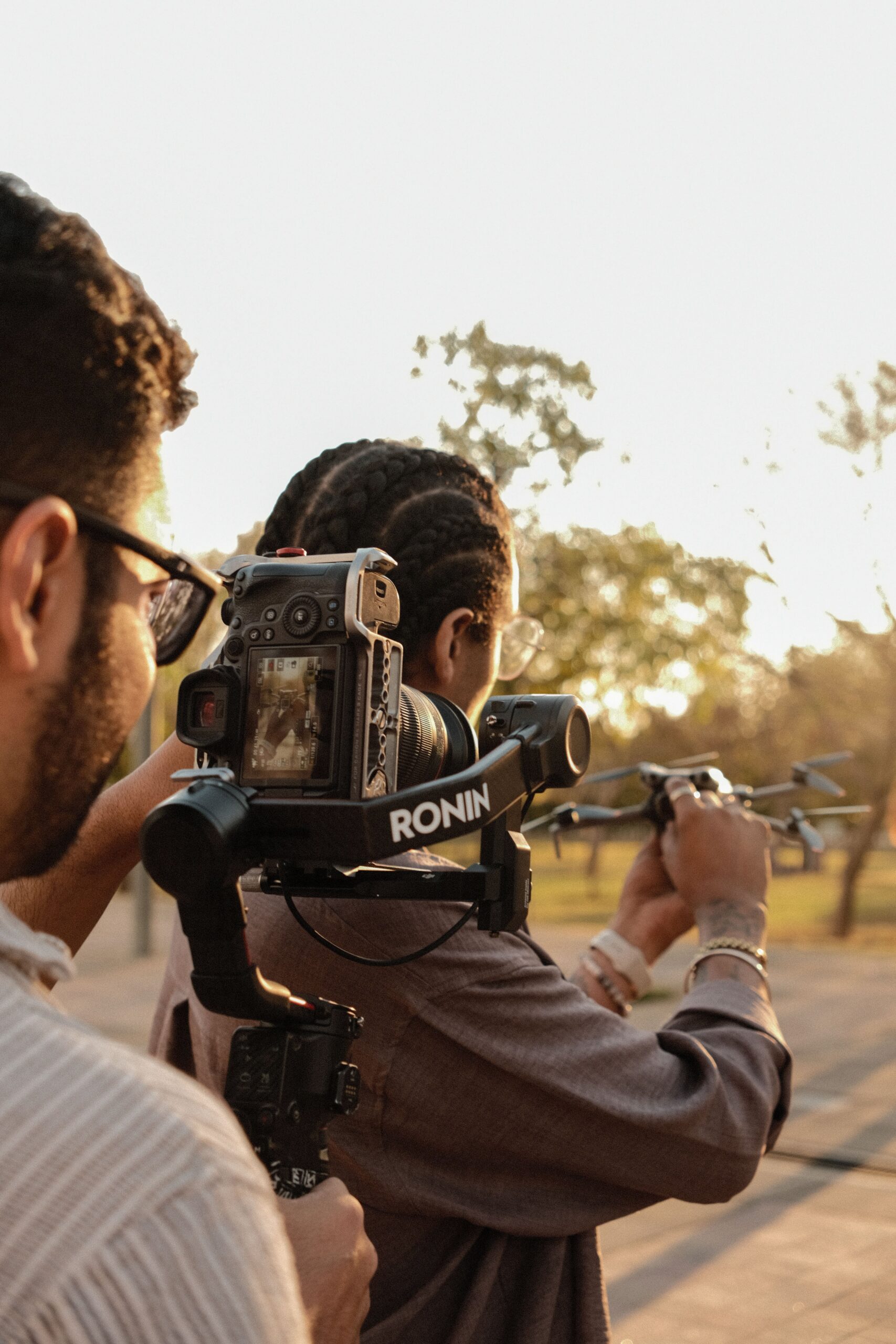 Two filmmakers using a gimbal for smooth footage outdoors during sunset.